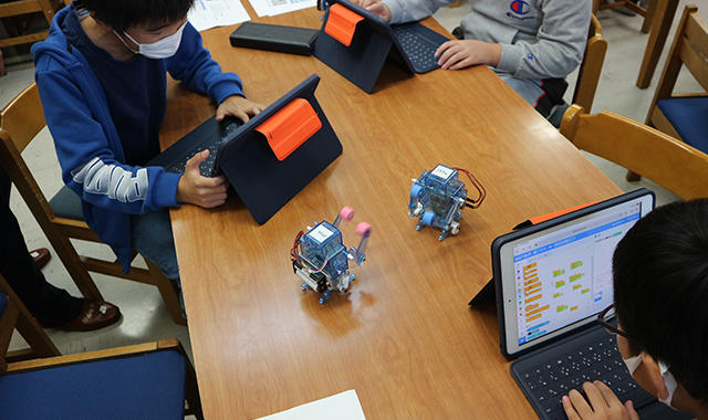 近隣地域の篠原小学校プログラミング部の生徒の皆さんに対して、ロボットを用いたプログラミング教室を実施している様子（写真3）